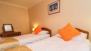 Ein Hotelzimmer mit zwei Betten, einem Nachttisch, einer Lampe und einem gerahmten Bild an der Wand.