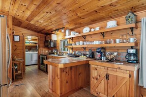 A wooden cabin interior with a kitchen area featuring a central island, wooden cabinets, and a coffee machine. - 10 Min to Downtown | Firepit + Pet Friendly (Blue Ridge)