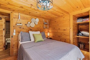 A wooden room with a bed, bedside table, and a shelf with board games. - 10 Min to Downtown | Firepit + Pet Friendly (Blue Ridge)