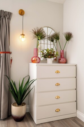 Une pièce avec une commode blanche, une plante en pot, un luminaire suspendu et un miroir doté d’un cadre en métal.