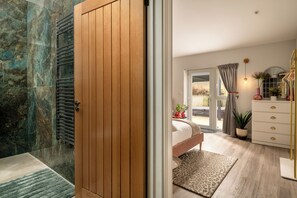 Ein Schlafzimmer mit Holztür, einem Bett, einem Schminktisch und Blick ins Freie.