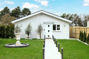 Una casa moderna de un solo piso con porche delantero, un pequeño jardín con una urna decorativa y una valla de madera.