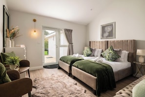 Un dormitorio moderno con una cama grande, una zona de estar con una silla, una mesita y una puerta que da a un espacio exterior.