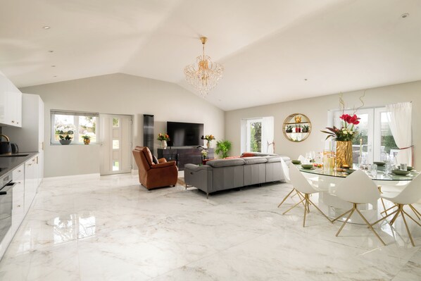 A spacious living area with a modern kitchen, a dining table set for six, and a large flat-screen TV. - Luxury 5* Retreat with pool spa & jacussi (Woodnesborough)