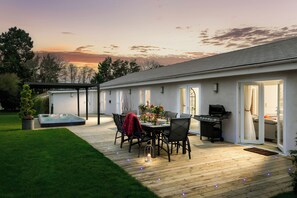Eine Terrasse im Freien mit Whirlpool, Esstisch und Stühlen, umgeben von einer Holzterrasse und einem Rasen.