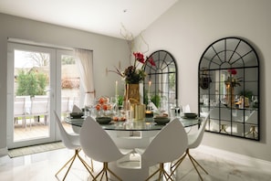 Un comedor con una mesa de vidrio, sillas blancas y un florero con flores.