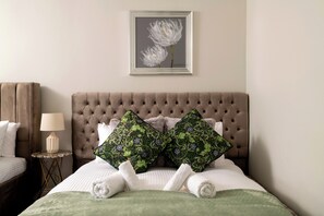 A neatly made bed with a tufted headboard, two decorative pillows, a framed artwork above, and a bedside table with a lamp. - Luxury 5* Retreat with pool spa & jacussi (Woodnesborough)