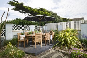 Un patio exterior con una mesa y sillas de madera, un paraguas grande y una cerca de piquetes blancos.