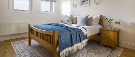 A bedroom with a wooden bed, a patterned rug, a nightstand, and a window with a view.