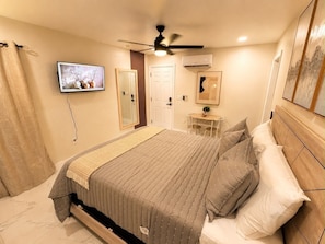A bedroom with a bed, a ceiling fan, a TV, a mirror, and an air conditioning unit. - Flora Luxe States (Tampa)