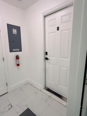 A white door with a black 'B' sign, a fire extinguisher, and a 'No Smoking' sign on a grey panel.