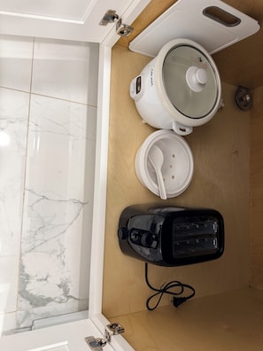 A kitchen with a coffee maker, a rice cooker, and a kettle on a wooden countertop.
