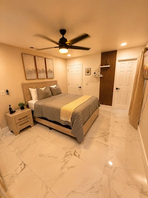 A bedroom with a bed, nightstand, ceiling fan, and artwork on the wall. - Flora Luxe States (Tampa)