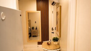 Un pasillo estrecho con un refrigerador blanco, una mesa de madera y una silla, y un espejo en la pared.