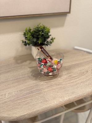 A clear glass bowl filled with assorted candies on a wooden surface.