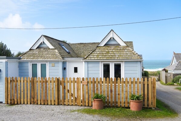 Een twee verdiepingen tellend strandhuis met een houten omheining, een grindpad en uitzicht op de oceaan.