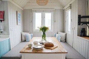Een eetruimte met een houten tafel, witte wanden en een raam met zonwering.