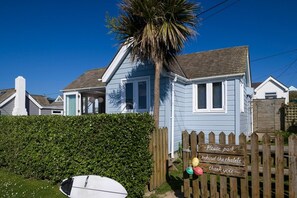 Een huis aan de kust met een houten omheining en een bordje waarop staat dat geparkeerd kan worden achter de chalets.