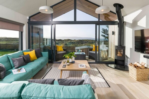 Een moderne woonkamer met een grote glazen deur die leidt naar een balkon, een zithoek, een salontafel en een open haard.