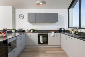 Eine moderne Küche mit grauen Schränken, einem eingebauten Backofen, einer Kaffeemaschine und einem Fenster, das natürliches Licht hereinlässt.