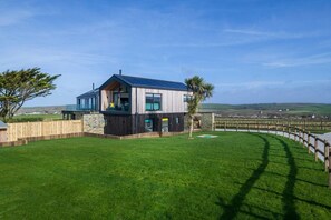 Een modern huis met een groot gazon, een houten terras en uitzicht op het landschap.