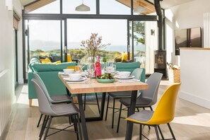 Een eetgedeelte met een tafel voor vier personen, omringd door moderne stoelen, een bank en uitzicht op het groen.