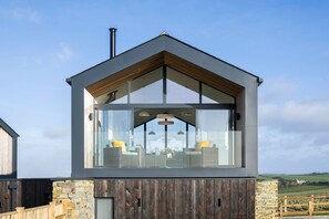 A modern building with a large glass window, wooden exterior, and a stone base. - Dune Lodge - sleeps 4 guests  in 2 bedrooms (Hayle)
