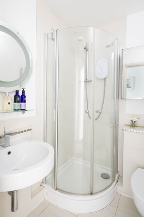 Een moderne badkamer met een douchecabine van glas, een witte wastafel en een spiegel boven de wastafel.
