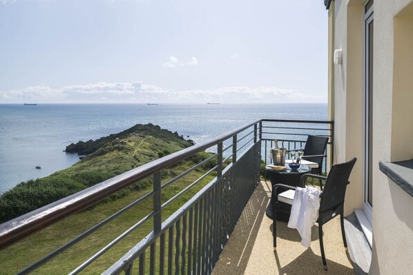 Een balkon met uitzicht op zee, een tafel met stoelen en een klein eiland in de verte.