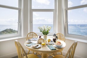 Een ontbijttafel met uitzicht op zee, een bloevas en een koffiepot.