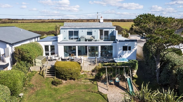 A two-story house with a patio area, a hot tub, and a swing set. - Fourburrows - sleeps 10 guests in 5 bedrooms (Mawgan Porth)