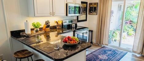 A kitchen with a central island, bar stools, a microwave, and a chandelier.