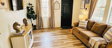 Un salon avec un plancher en bois, un canapé marron, un ventilateur de plafond et une porte.