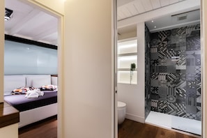 A modern hotel room with a bed, a bedside table, a small window, and a bathroom with a toilet and sink. - Old Town Prestige Loft by Flatinrome (ROMA)