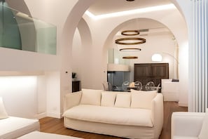A modern living room with a sofa, a dining area with chairs, and a kitchen in the background. - Old Town Prestige Loft by Flatinrome (ROMA)