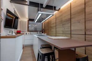 A modern kitchen with a long countertop, bar stools, and a built-in oven. - Old Town Prestige Loft by Flatinrome (ROMA)