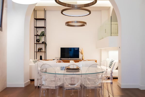 A modern dining area with a glass table and chairs, a flat-screen TV, and a minimalist shelving unit. - Old Town Prestige Loft by Flatinrome (ROMA)