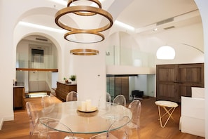 A modern dining area with a glass table and chairs, a chandelier, and a view of a kitchen and living space. - Old Town Prestige Loft by Flatinrome (ROMA)