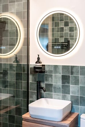 Een badkamer met een wit wastafel, een ronde spiegel en een handzeepdispenser op een zwarte houder.