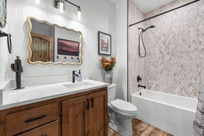 A bathroom with a white sink, wooden cabinets, a toilet, and a bathtub. - The Perch – Brand New Zion Retreat with Hot Tub (Orderville)