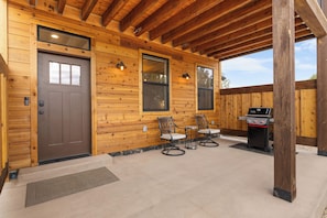 Un patio couvert avec une structure extérieure en bois, un barbecue et deux chaises.