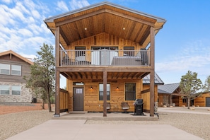 Une cabane en bois à deux étages, dotée d’un balcon, d’une porte d’entrée et d’un espace barbecue.