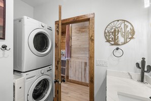 Una lavanderia con lavatrici affiancate, una porta in legno e una decorazione a forma di cactus appesa al muro.