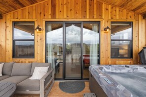 A wooden cabin interior with a sofa, a bed, and a sliding glass door leading to a balcony. - The Perch – Brand New Zion Retreat with Hot Tub (Orderville)