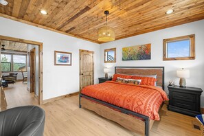 Une chambre avec un plafond en bois, un lit recouvert d’une couverture orange, une table de chevet avec une lampe et un tableau accroché au mur.