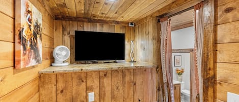 A wooden-paneled room with a television on a shelf, a fan, and a bed with a floral pattern.