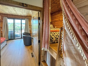 A wooden cabin with a balcony, a bed with floral bedding, and a view of the outdoors. - The Perch – Brand New Zion Retreat with Hot Tub (Orderville)