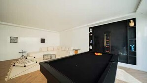 Ein modernes Wohnzimmer mit Billardtisch, einer Couch und einem dekorativen Teppich.