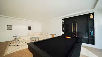 A modern living room with a pool table, a sofa, and a decorative rug.