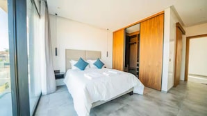 Ein modernes Schlafzimmer mit einem großen Bett, einem begehbaren Kleiderschrank und Blick durch ein großes Fenster.